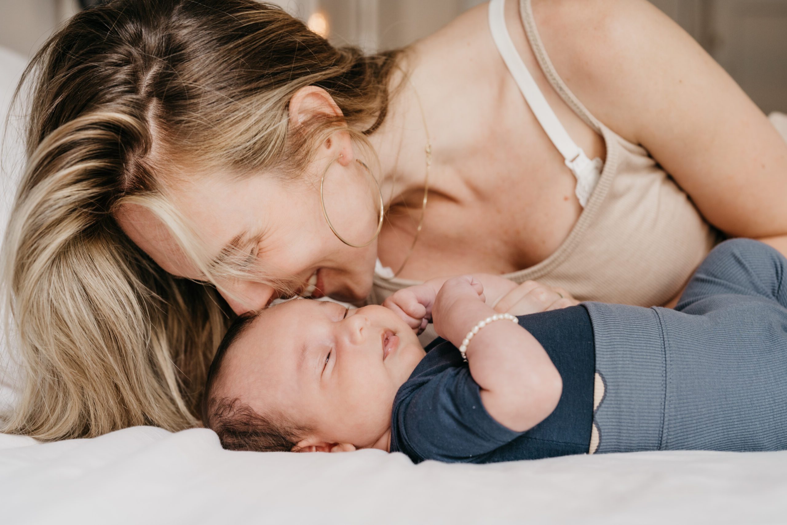 moeder ligt op bed en geeft newborn baby een kus op zijn voorhoofd