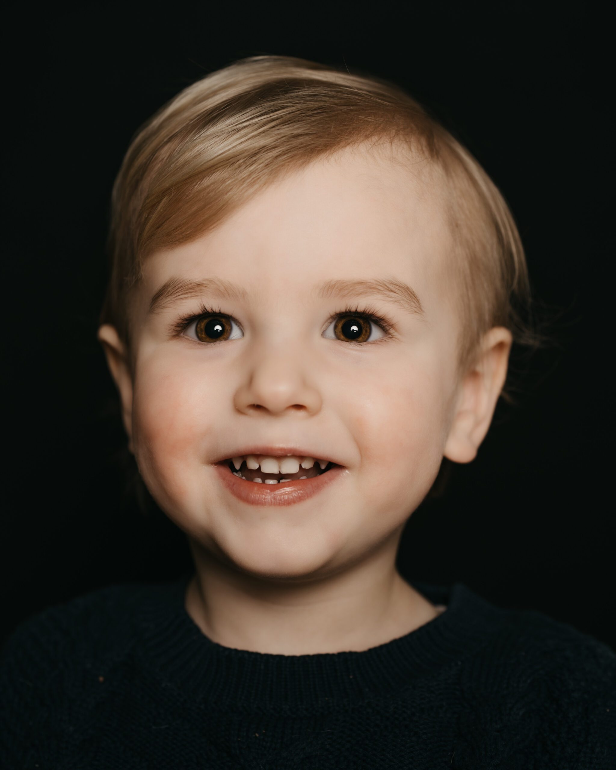 Fine art kinderportret van een lachend jongetje met mooie ogen voor een zwarte achtergrond